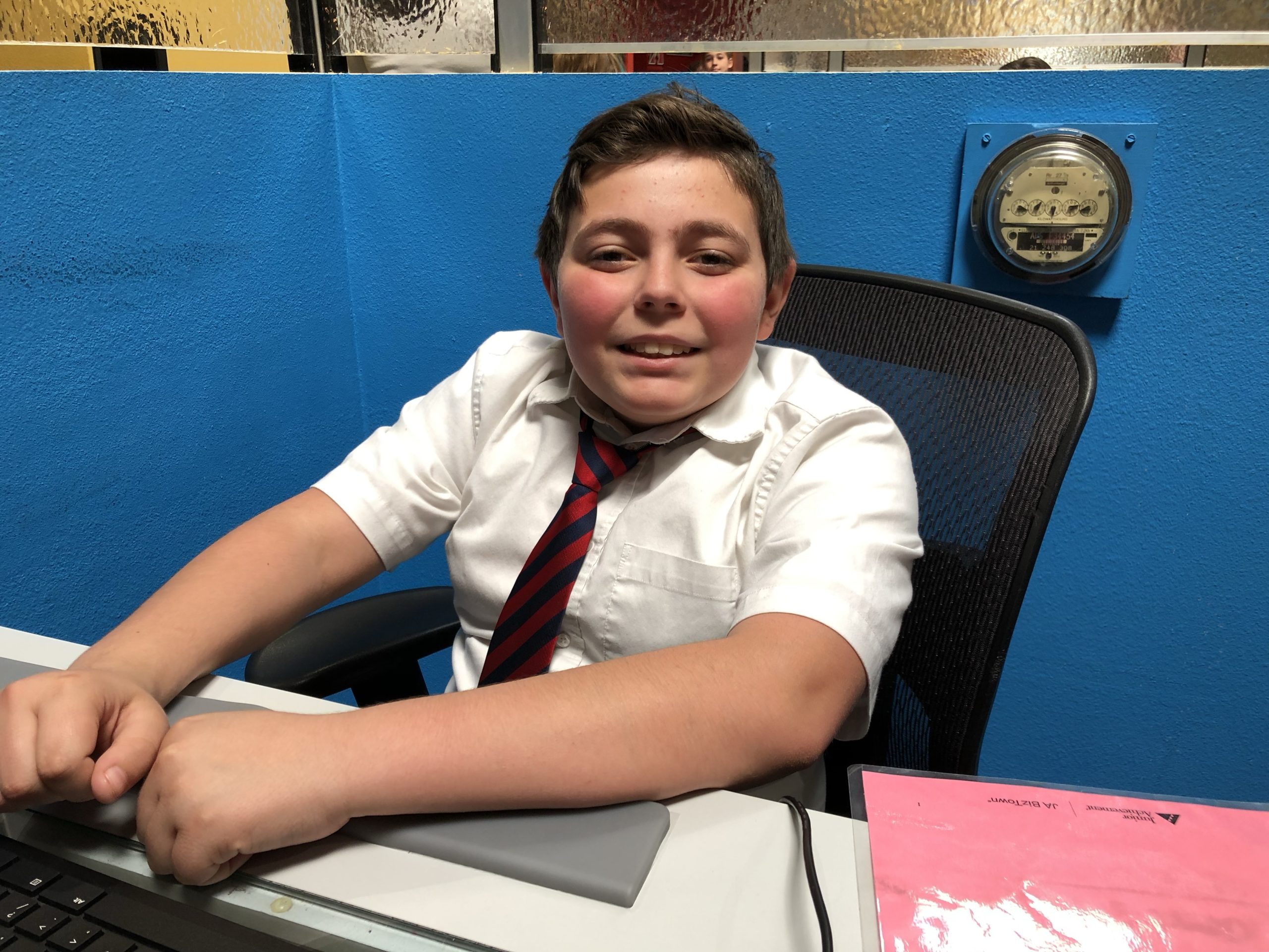 young boy sitting at desk wearing a tie