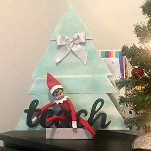 Christmas elf sitting on "teach" sign
