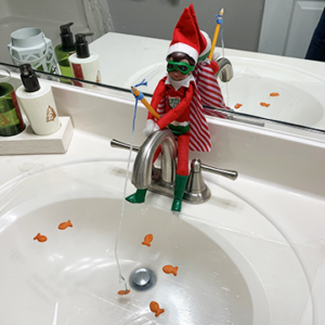 Christmas elf sitting on sink faucet fishing for goldfish