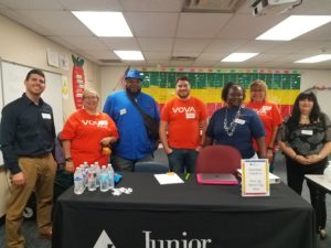 Adult JA volunteers standing behind JA table